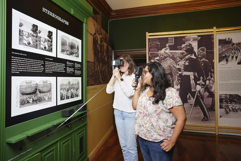 Indian Army at the Palace exhibition 2023, showing Sophie Lemagnen (Media & PR Manager) and Zakira Begum (Interpretation Officer) interacting with the exhibits. The 2023 Indian Army at the Palace exhibition explores the forgotten story of Indian Army soldiers who camped at Hampton Court Palace in the early 20th century, through a display of previously unseen objects, photographs, film and personal stories.